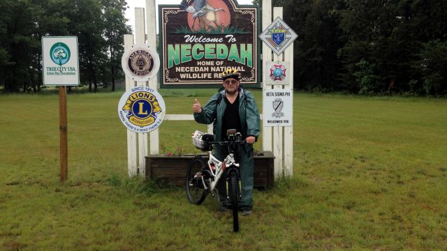 paul and bike in front of welcome to Neceedah sign.