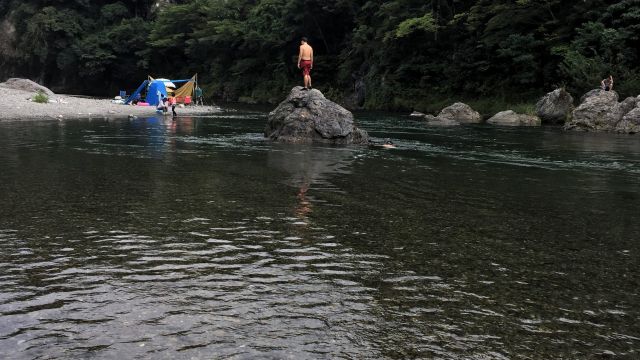 A swimmer standing on a rock in the middle of the Tama River.