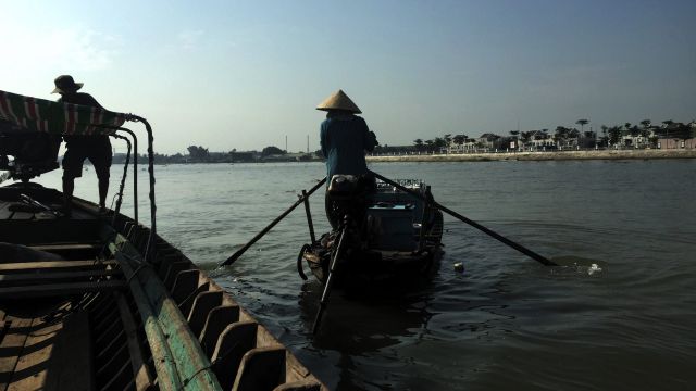 Woman on small boat rowing away from larger sampan