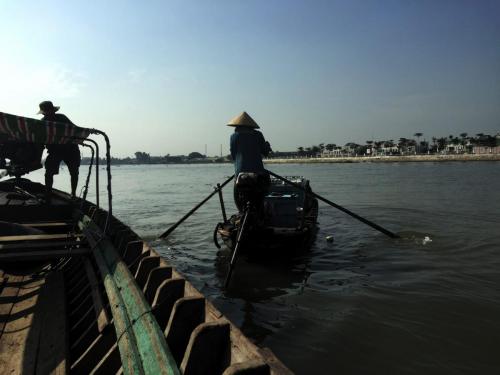 Woman on small boat rowing away from larger sampan